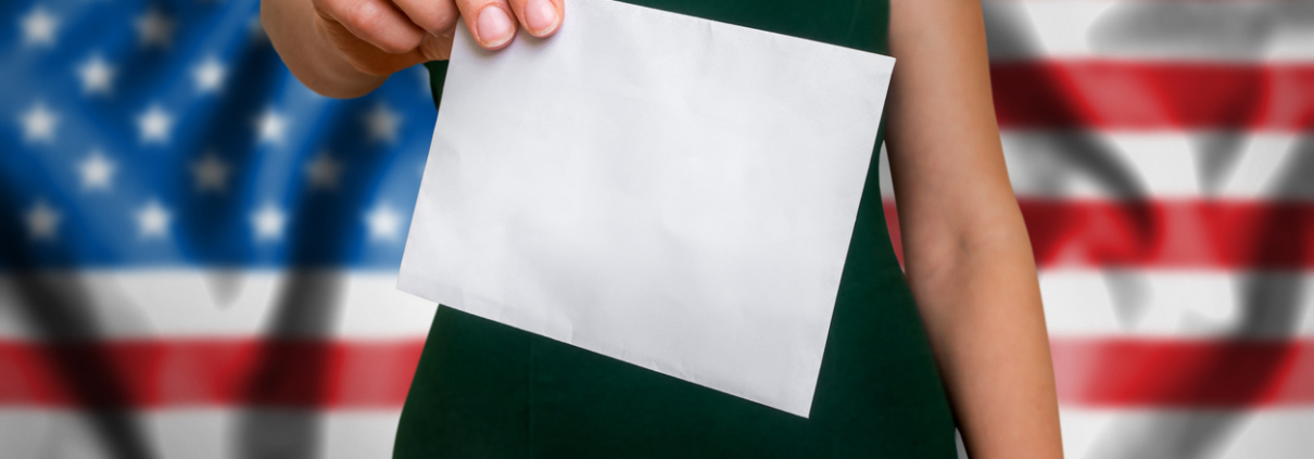 Election in United States of America - voting at the ballot box. The hand of woman putting her vote in the ballot box. Flag of USA on background.