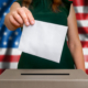 Election in United States of America - voting at the ballot box. The hand of woman putting her vote in the ballot box. Flag of USA on background.