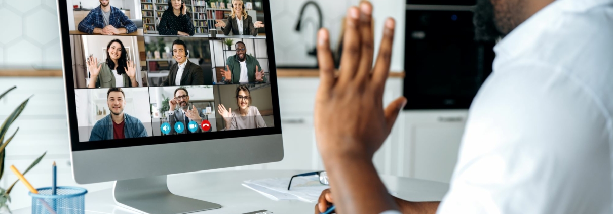 Working IDEAL blog about fair pay by geographic location | Image features a man working remotely at home on a video meeting with colleagues on the screen