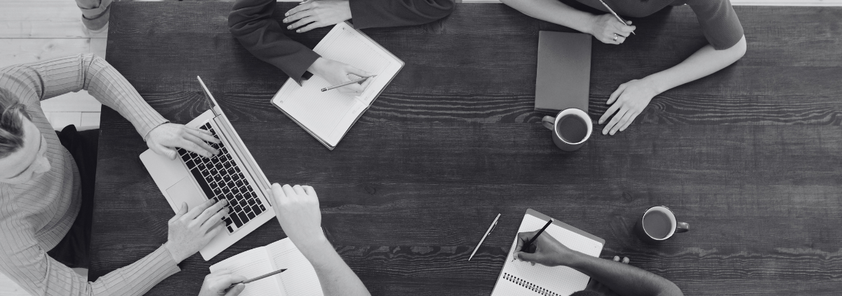 colleagues meeting in an office around a dark wood table with notepads and a laptop