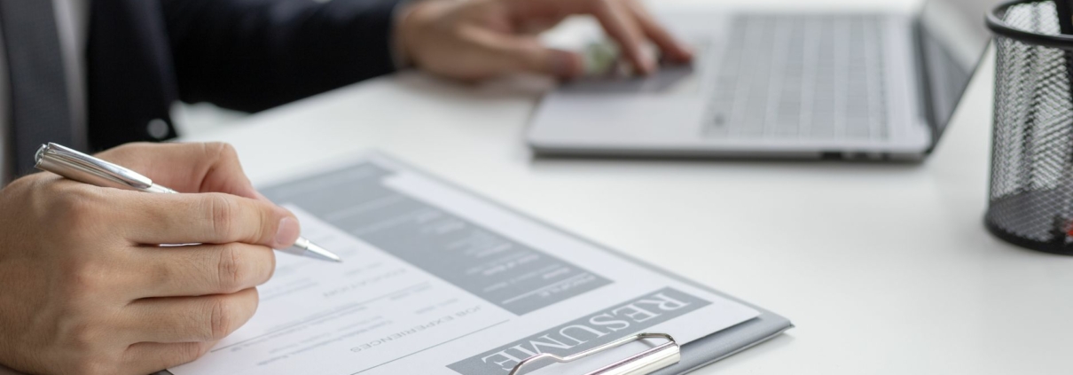 Working IDEAL blog about pay equity - image shows a person reviewing a resume with a laptop on the table