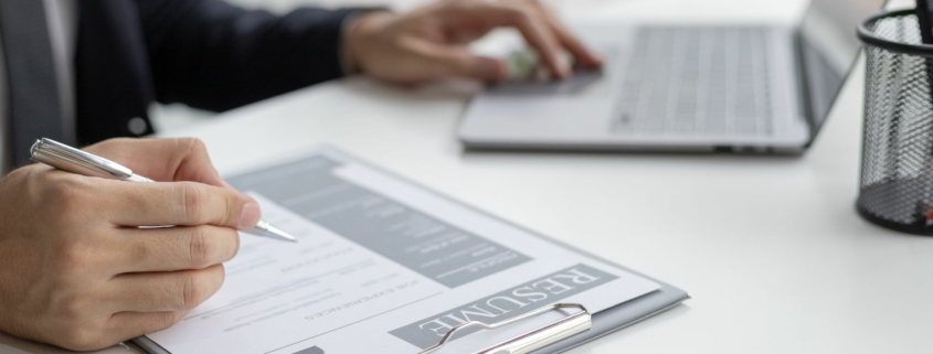 Working IDEAL blog about pay equity - image shows a person reviewing a resume with a laptop on the table